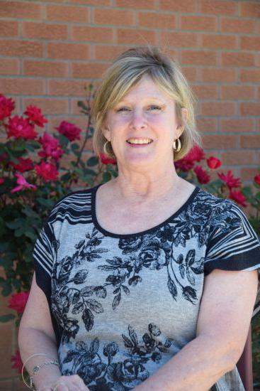 Connie Browning stands against a rose-vined exterior brick wall.